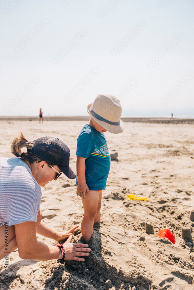 Mother covers her sons feet with sand at the beach. Mother covers her sons feet with sand at the beach.