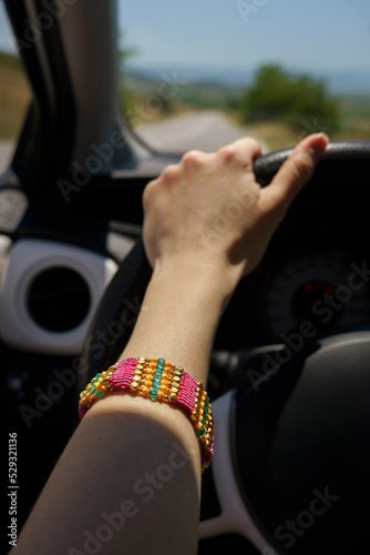 Female hand with pink bracelet on steering wheel. Road trip