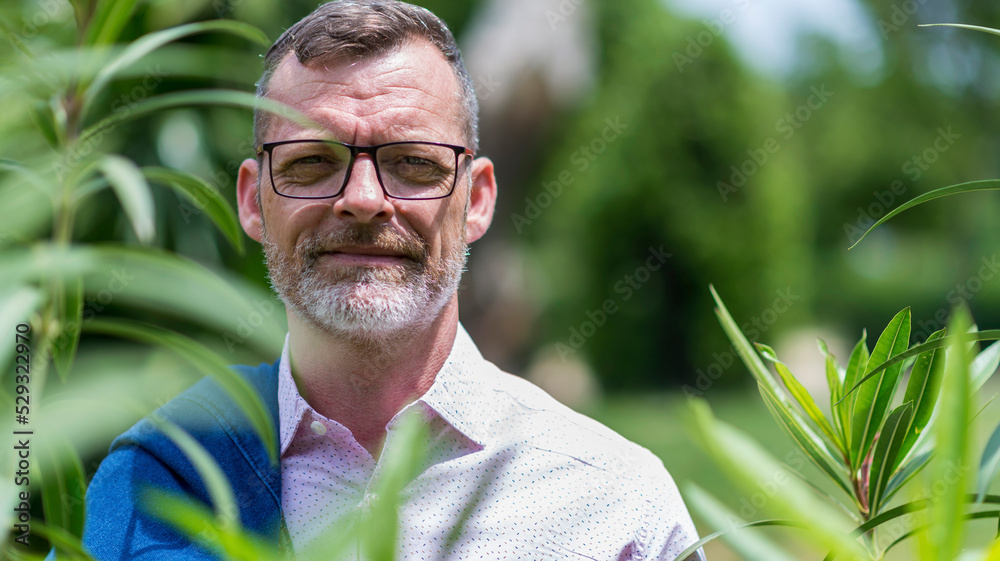 Front view of bearded adult man hidden behind foliage looking camera Front view of bearded adult man hidden behind foliage looking camera