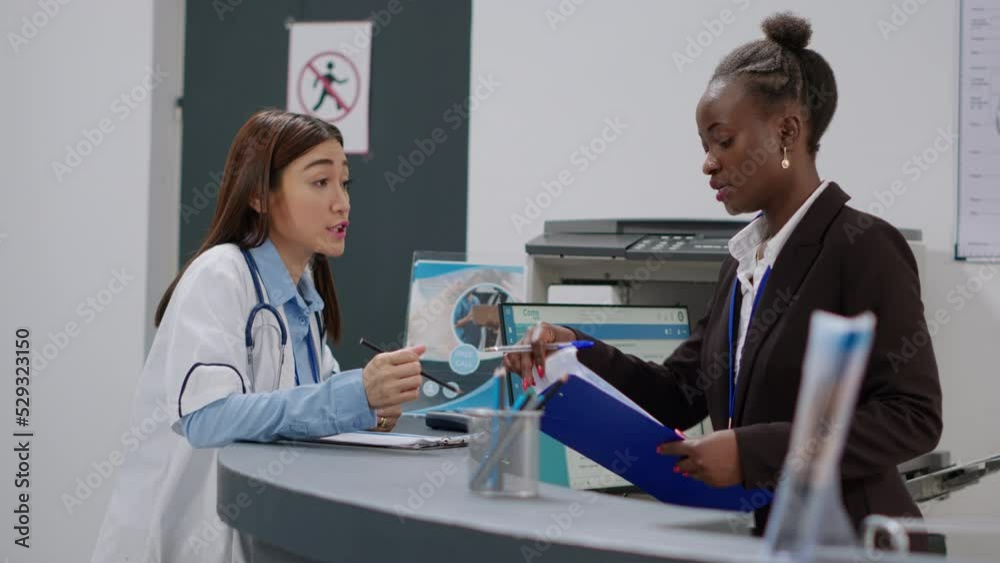 Diverse team of doctor and receptionist working at reception desk to fill in medical report papers and make healthcare appointments. Medical staff doing registration work in facility lobby.
