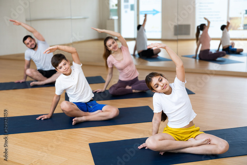 Fit woman, man and teenage girl and boy performing yoga exercises on gymnastic mats at yoga studio, physical, emotional and spiritual family health concept