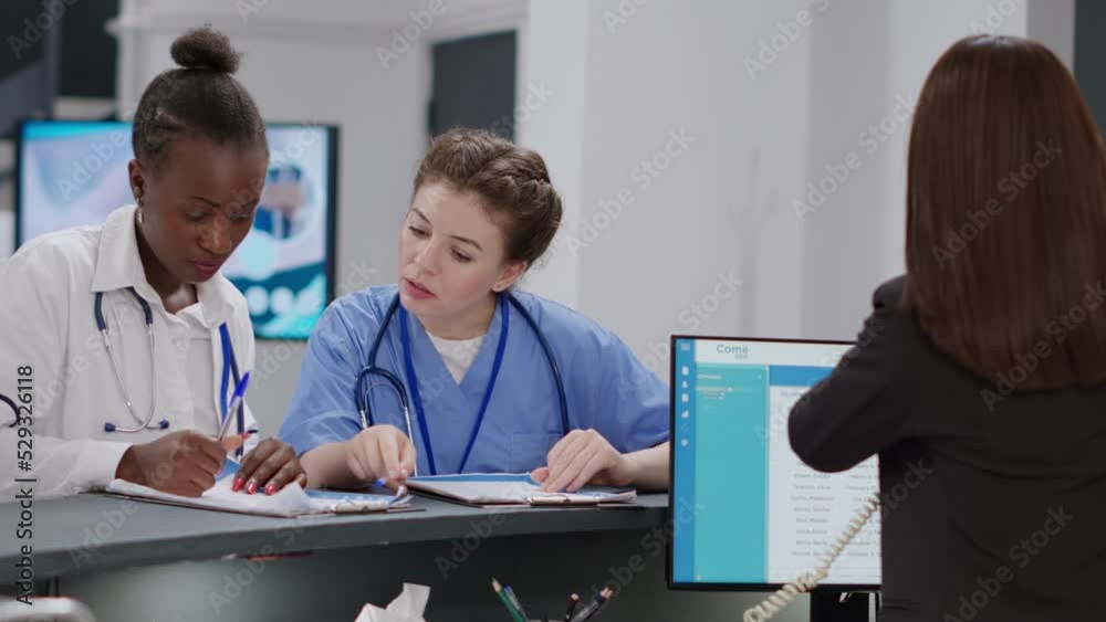 Diverse medical team working at hospital reception desk ith receptionist, analyzing checkup papers to help with healthcare appointments. Specialists writing insurance report at registration counter.