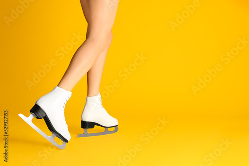 Woman in elegant white ice skates on yellow background, closeup of legs. Space for text