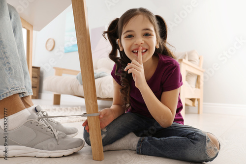 Vászonkép Cute little girl tying shoe laces of her father together at home, closeup