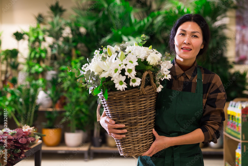 Fototapeta premium Portrait of a confident and successful Asian florist woman standing in a shop with flowers in her hands