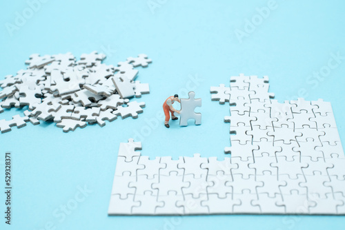水色背景に白いパズルを組み立てる一人の作業員のフィギア