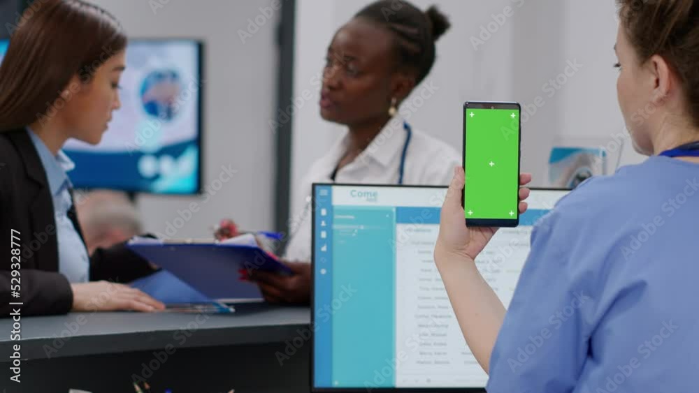 Medical assistant holding smartphone with greenscreen display at hospital reception counter. Nurse using chroma key template with isolated mockup background and blank copyspace. Medical assistant holding smartphone with greenscreen display at hospital reception counter. Nurse using chroma key template with isolated mockup background and blank copyspace.