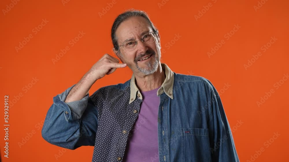 Happy fun mature man 50s point finger and doing phone gesture like says call me back isolated on solid orange background studio portrait Happy fun mature man 50s point finger and doing phone gesture like says call me back isolated on solid orange background studio portrait