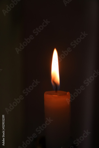 Defocus close up single candle light and flame on black background. Vertical. RIP flame. Memory. Out of focus