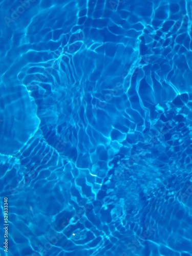 Bluewater waves on the surface ripples blurred. Defocus blurred transparent blue colored clear calm water surface texture with splash and bubbles. Water waves with shining pattern texture background.