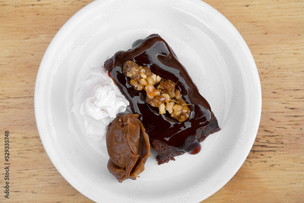 Sweet desserts. Top view of a bittersweet chocolate flan with vanilla cream and dulce de leche, in a white dish on the wooden table. Sweet desserts. Top view of a bittersweet chocolate flan with vanilla cream and dulce de leche, in a white dish on the wooden table.