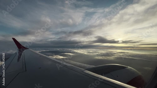 Passenger seat window point of view airplane wing and engine with cloudscape panorama early morning with and sunrise view behind clouds photo