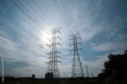 A picture of electric transmission tower and line with cloud and sunlight at the back during daytime.