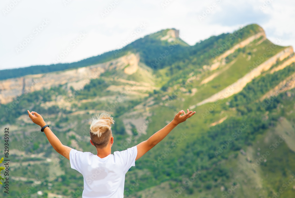 A boy looking at the mountains and spreading his arms to the sides against the background of the mountains A boy looking at the mountains and spreading his arms to the sides against the background of the mountains