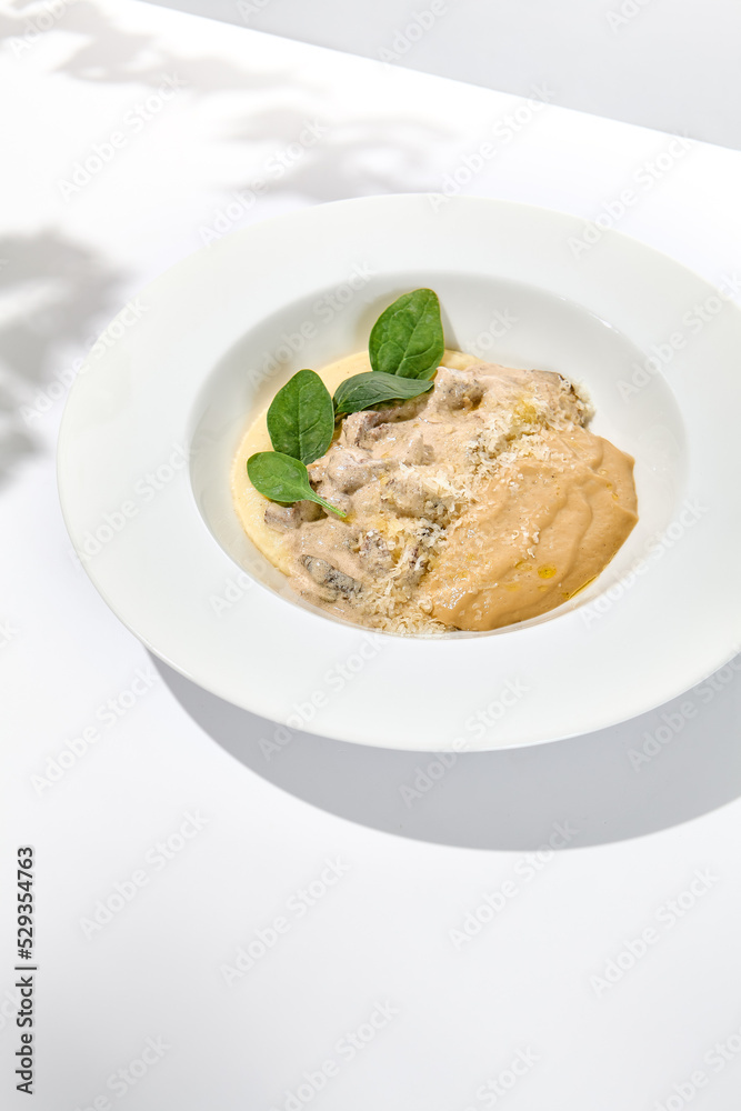 Traditional russian food - beef stroganoff with mushroom sauce and mashed potatoes. Beef stroganoff in white plate on light background with hard shadows. Stew meat with creamy sauce on summer menu.