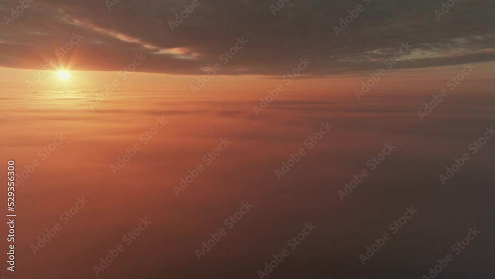Slow aerial pan of sun shining above thick cloud cover during brilliant sunrise.