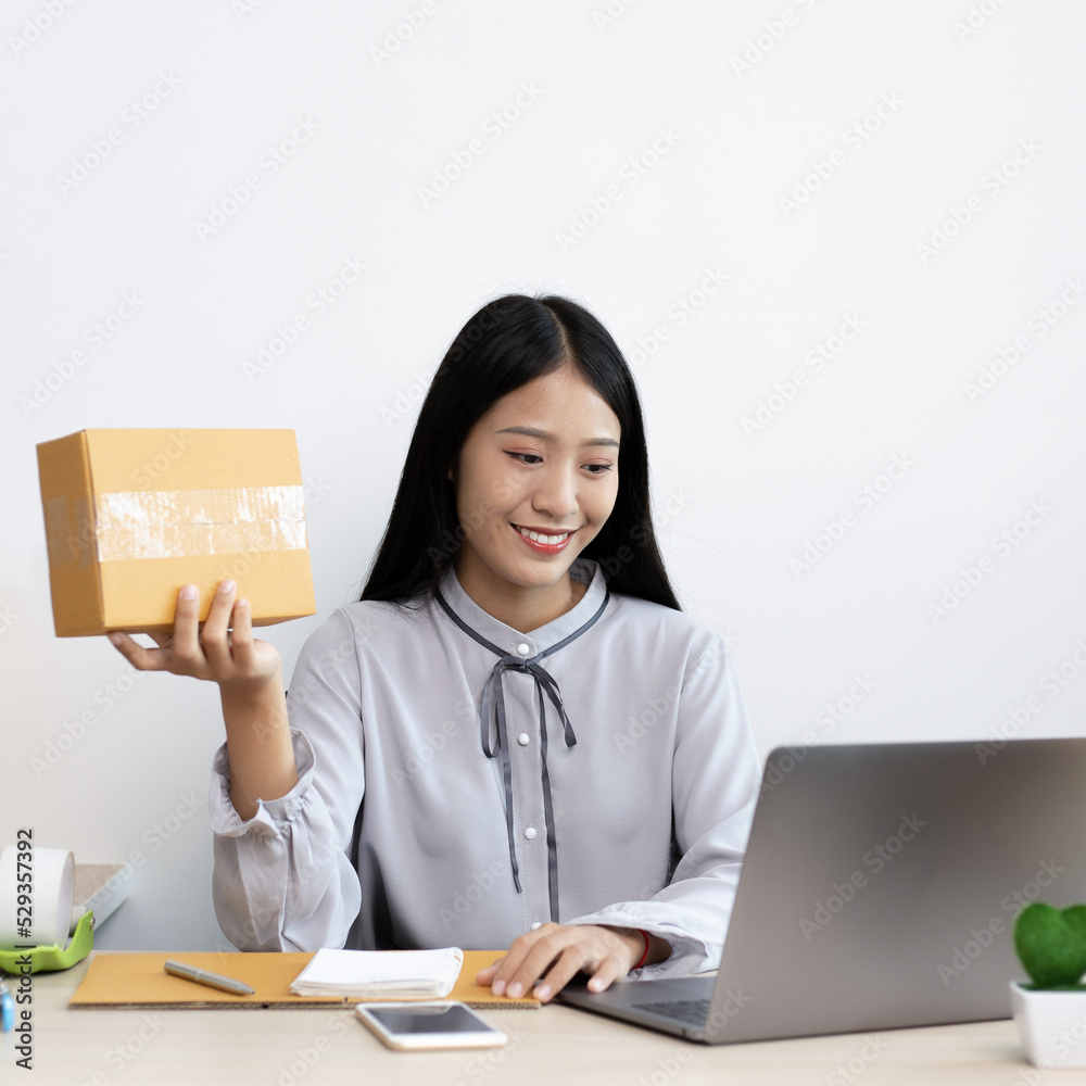 Young Asian woman chatting with a customer on a laptop and displays the product before delivery to confirm the order, Selling products online or doing freelance work at home concept. Young Asian woman chatting with a customer on a laptop and displays the product before delivery to confirm the order, Selling products online or doing freelance work at home concept.