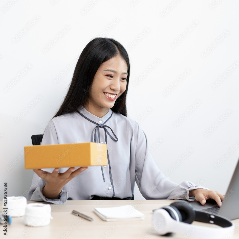 Young Asian woman chatting with a customer on a laptop and displays the product before delivery to confirm the order, Selling products online or doing freelance work at home concept. Young Asian woman chatting with a customer on a laptop and displays the product before delivery to confirm the order, Selling products online or doing freelance work at home concept.