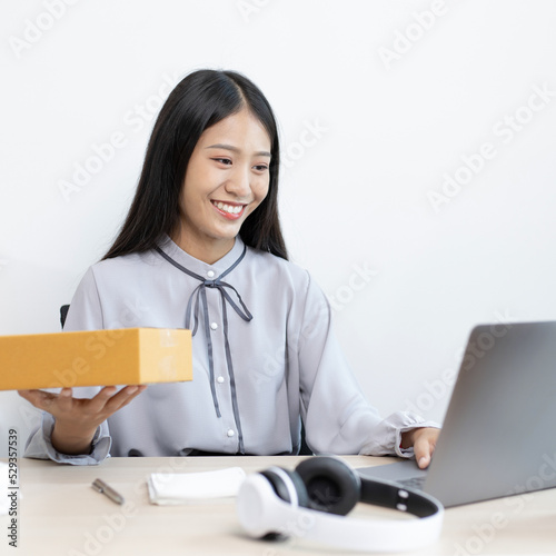 Young Asian woman chatting with a customer on a laptop and displays the product before delivery to confirm the order, Selling products online or doing freelance work at home concept. photo