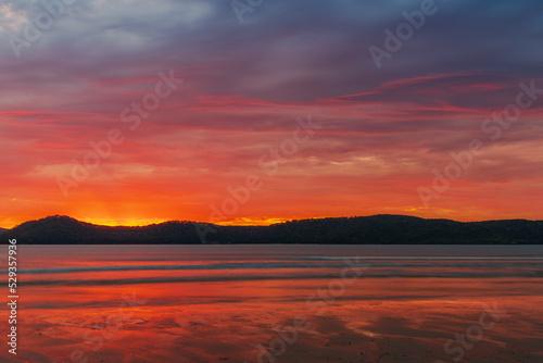 Colourful cloud filled sunrise at the seaside © Merrillie