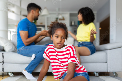 Divorce And Domestic Violence. Portrait of upset African American daughter looking through the window while her angry parents fighting in the background, depressed child feeling lonely