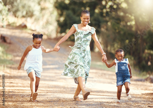 Happy, mother and kids walking in a forest holding hands in nature in joyful happiness and smiling. Black family of a mom and her little girls bonding on a fun walk in the natural outdoor environment