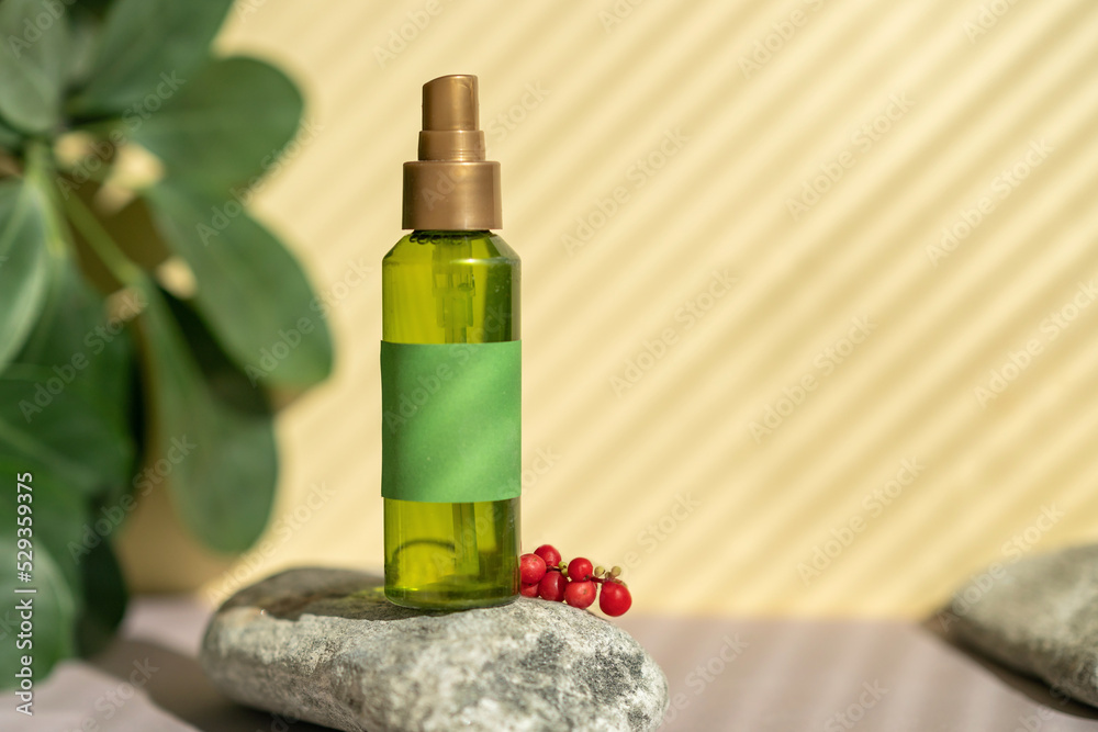 A bottle of green color with a spray bottle lies on the stones, next to the green leaves and berries of schisandra chinensis