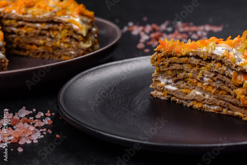 Delicious fresh liver cake with mayonnaise and carrots on a black plate against a dark concrete background