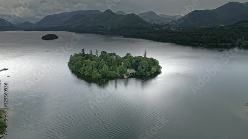 Drone Aerial footage of a Island and  house on Derwentwater, Keswick, a calm lake with river boats and a stormy sky. Surrounded by mountain's, hills and lush woodland. photo