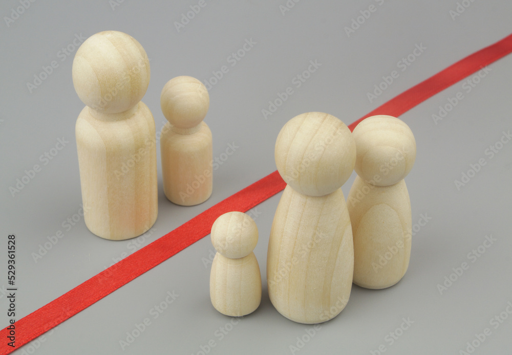 Family members separated by border. Father with son wooden figures separated from wife and daughters figures. Problems with visas for family members and citizenship concept.