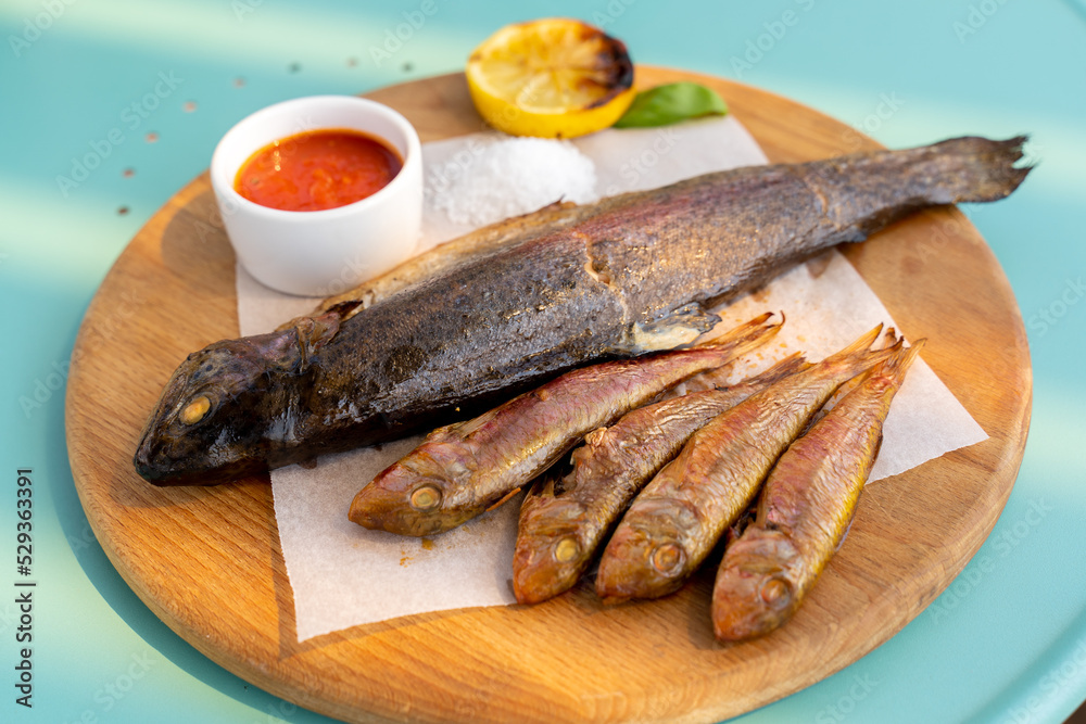 Large and small fried fish on a wooden board, Sauce, salt. close-up. Large and small fried fish on a wooden board, Sauce, salt. close-up.