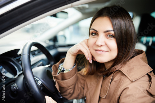 Attractive young woman smiling and looking at the camera while driving her new car to work