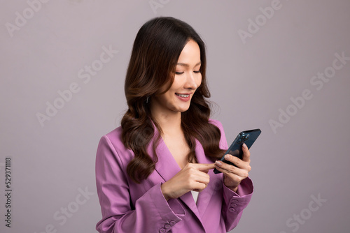 Beautiful Asian womaa using smartphone standing isolated on gray background. Shopping online mobile phone.