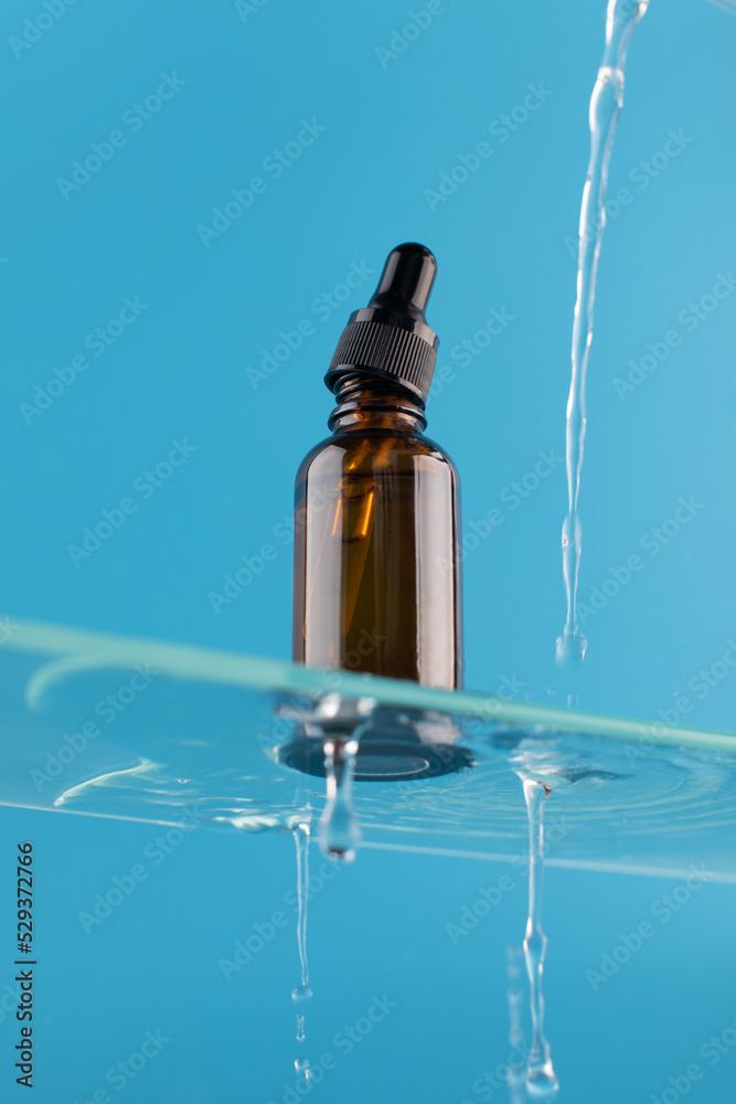  A brown dropper with a cosmetic product, with a serum for facial skin on a glass shelf with water splashes. 