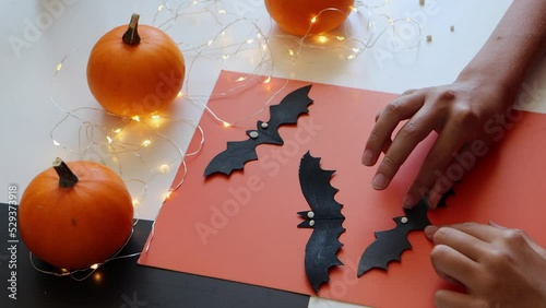 selective focus on the child's hands holding a black bat cut out of cardboard, a decoration for the Halloween holiday.