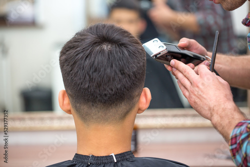 Male hairdresser, grooming men. Haircut styler and trimmer. The master cuts a man, shaves his temples and neck. The client at the hairdresser looks in the mirror. barbershop photo