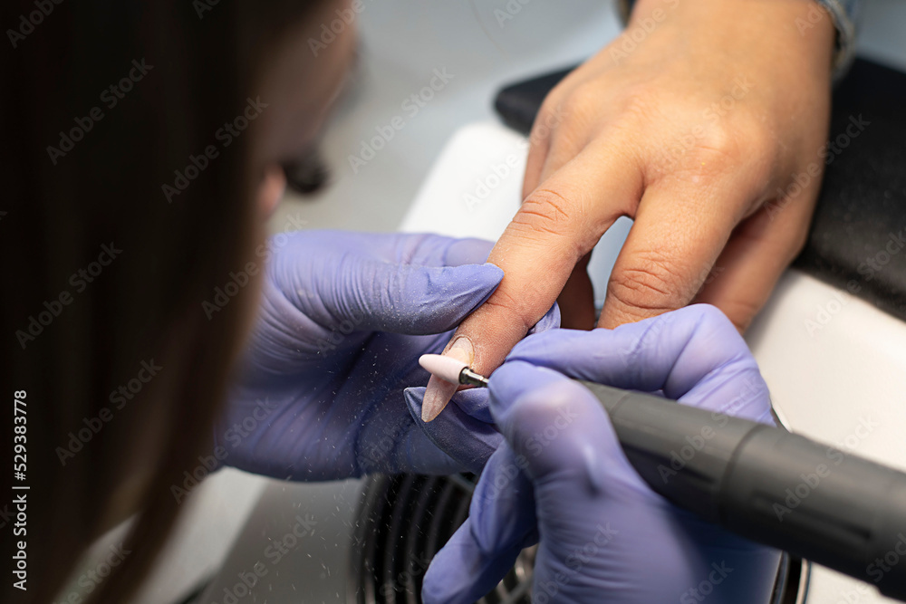 Manicurist in lilac latex gloves removes yellow gel polish to a client in a beauty salon