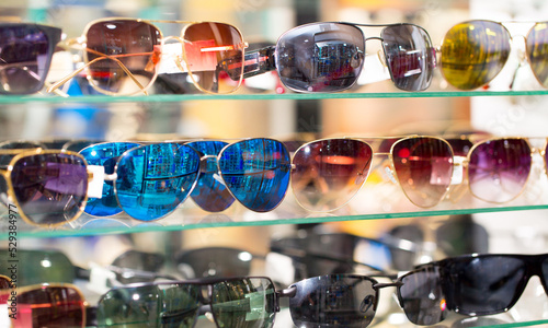 Sunglasses on optics shelves. Large selection of glasses for vision correction. The glasses are laid out on the store's glass shelves in neon lighting.