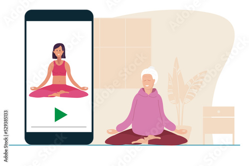 Online yoga. Elderly woman sitting in lotus position doing meditation on mat at home. Woman watches at yoga lessons on your phone. Yoga, meditation, relax, recreation, healthy lifestyle in old age.