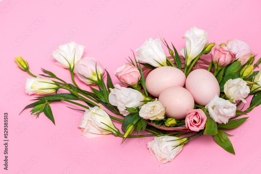 Obraz premium Easter background with Easter eggs and spring flowers. Top view with copy space. Nest with eggs decorated with beautiful flowers on a pink background.