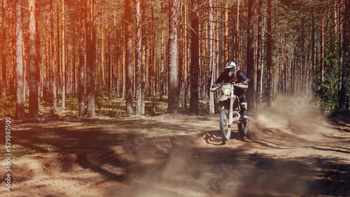motorcycle racer on an enduro sports motorcycle rides fast on a dusty road in the forest in an off-road race on a sunny day
