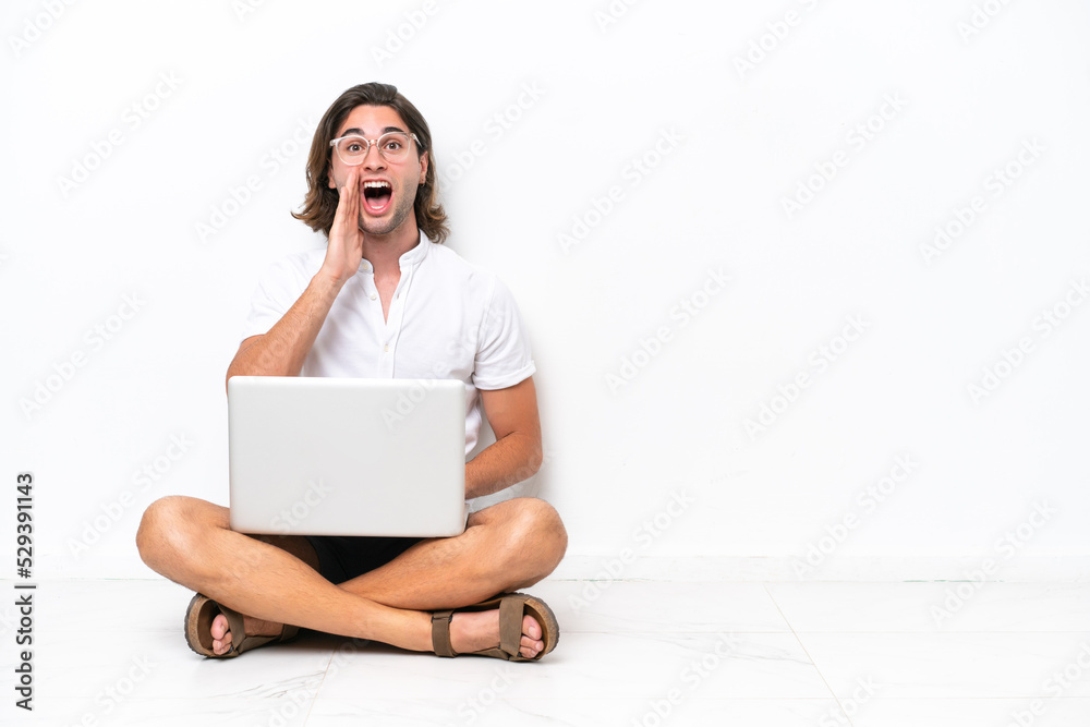 Young handsome man with a laptop sitting on the floor isolated on white background with surprise and shocked facial expression Young handsome man with a laptop sitting on the floor isolated on white background with surprise and shocked facial expression