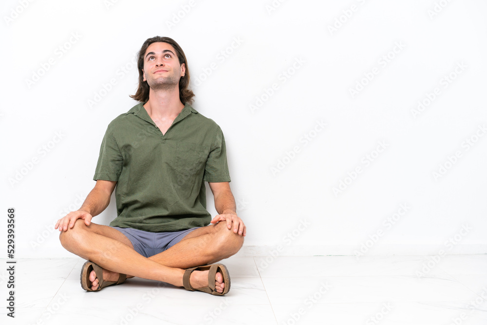 Young handsome man sitting on the floor isolated on white background and looking up Young handsome man sitting on the floor isolated on white background and looking up