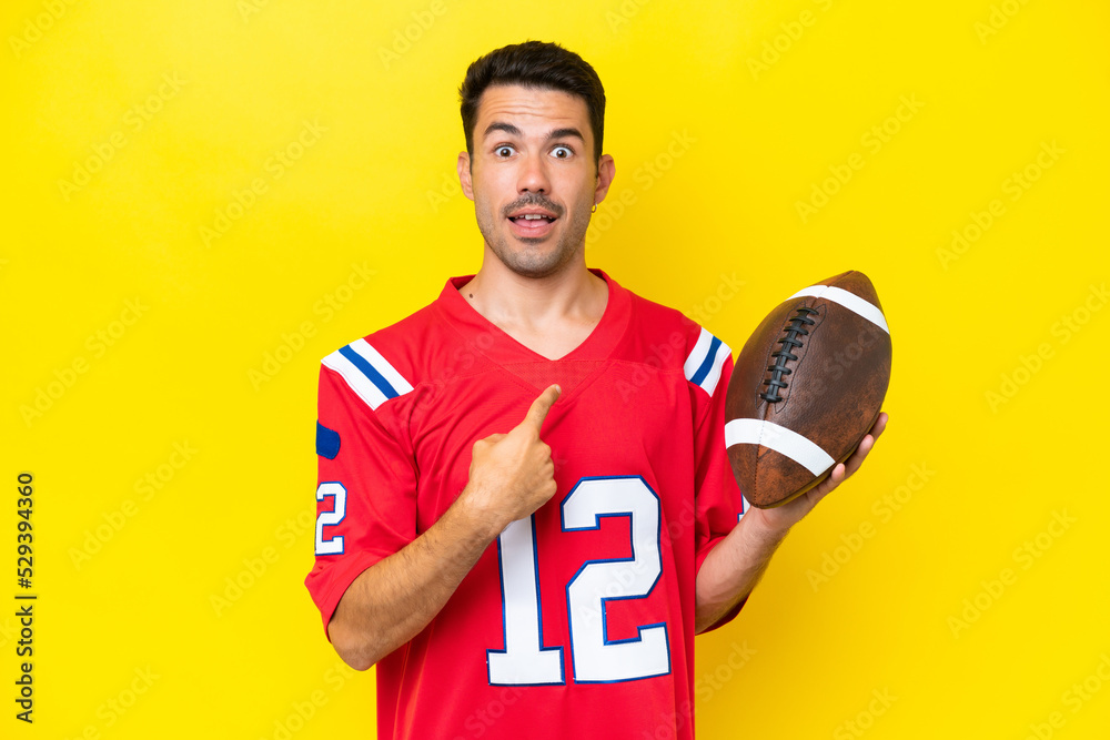 Young handsome man playing rugby over isolated yellow background with surprise facial expression Young handsome man playing rugby over isolated yellow background with surprise facial expression