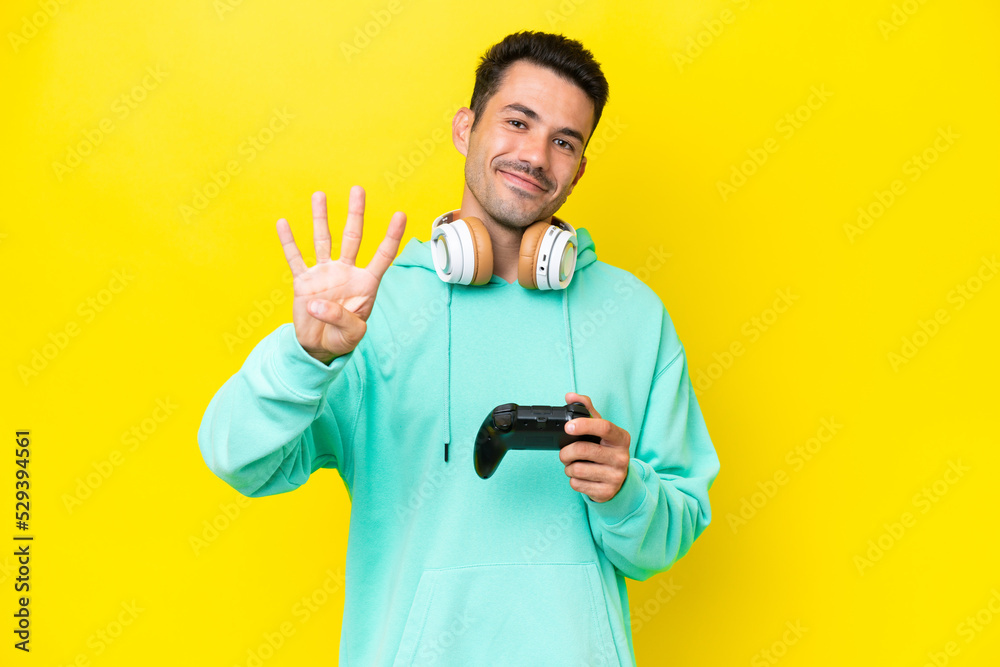 Young handsome man playing with a video game controller over isolated wall happy and counting four with fingers