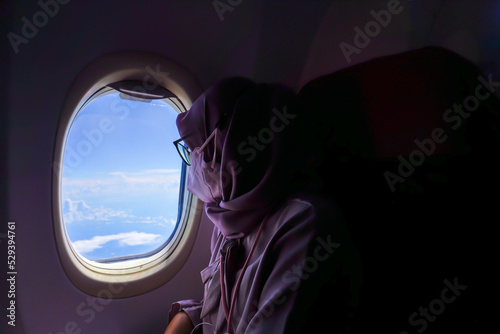 A female passenger is looking at the view of the blue sky from the cabin of the plane.