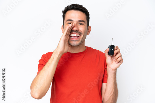 Young handsome man holding car keys over isolated white background shouting with mouth wide open