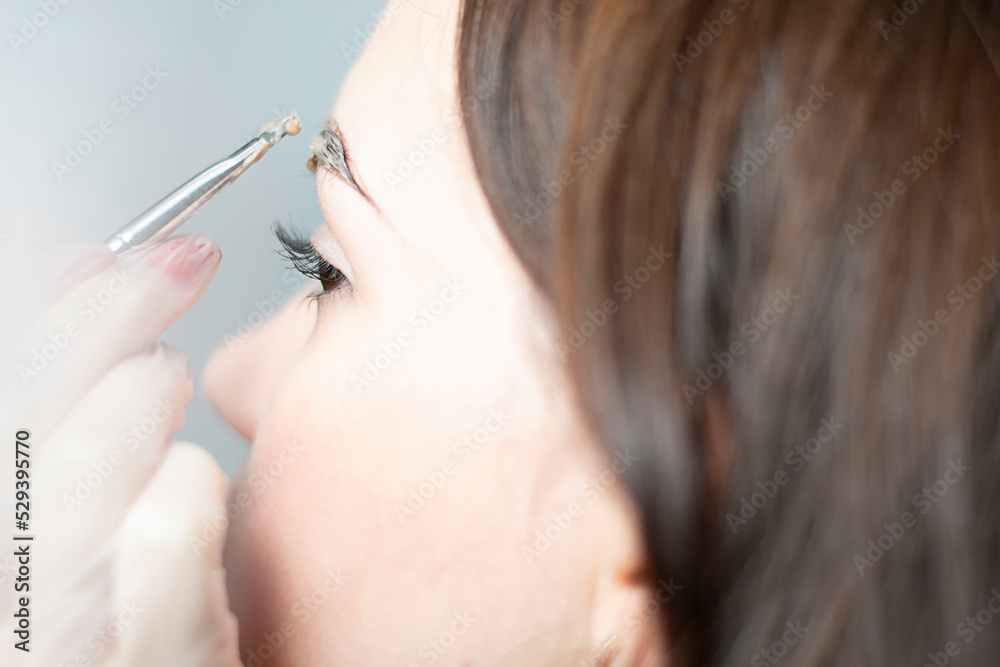 The master dyes the eyebrows brown to a beautiful young Caucasian girl. Close-up.