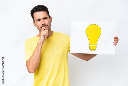 Young handsome man over isolated white background holding a placard with bulb icon and thinking