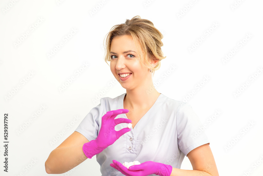 Portrait of a young smiling Caucasian beautician wearing pink gloves holding sugar cubes showing and looking at the camera against a white background Portrait of a young smiling Caucasian beautician wearing pink gloves holding sugar cubes showing and looking at the camera against a white background